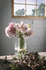 Table en bois avec bouquet de chrysanthèmes roses dans un vase entre pétales tombés et mur blanc avec fenêtre — Photo de stock