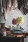 Дерев'яний стіл з купою свіжих рожевих хризантем та білою гортензією у вазі між сковородою та посудом біля посуду, що звисає на скручених штифтах — стокове фото