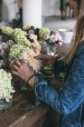 Glückliche Dame am Holztisch mit Sträußen frischer Chrysanthemen, Rosen und Pflanzenzweigen in Vasen auf grauem Hintergrund — Stockfoto