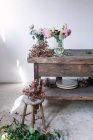 Дерев'яний стіл з посудом і букетами свіжих квітів у вазах з водою біля білої стіни — стокове фото