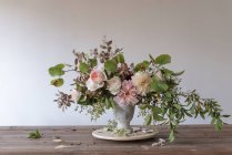 Concept of bouquet of dry and fresh roses, chrysanthemums and plant twigs in retro vase on wooden board on grey background — Stock Photo