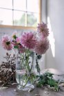 Wooden table with kitchenware and bouquets of fresh blooms in vases with water near white wall — Stock Photo