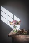 Wooden table with bouquet of pink chrysanthemums in vase between fallen petals and white wall with sunshine — Stock Photo