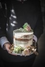 Vista lateral da colheita alegre senhora segurando prato com bolo saboroso decorado por botão crisântemo e folhas secas no quarto — Fotografia de Stock