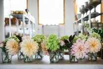 Дерев'яний стіл з посудом і букетами свіжих квітів у вазах з водою біля білої стіни — стокове фото