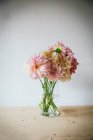 Дерев'яний стіл з посудом і букетом свіжих квітів у вазі з водою біля білої стіни — стокове фото