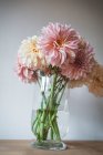 Tavolo in legno con stoviglie e mazzo di fiori freschi in vaso con acqua vicino alla parete bianca — Foto stock