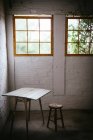 Conceito de mesa perto de banquinho em quarto cinza escuro com paredes de tijolo — Fotografia de Stock