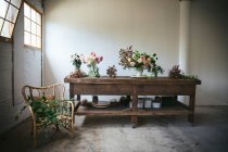 Tavolo in legno con stoviglie e mazzi di fiori freschi in vasi con acqua vicino alla parete bianca — Foto stock