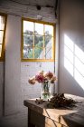 Table en bois avec ustensiles de cuisine et bouquets de fleurs fraîches dans des vases avec de l'eau près du mur blanc — Photo de stock