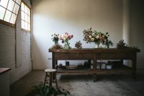 Holztisch mit Geschirr und Sträußen frischer Blüten in Vasen mit Wasser in der Nähe der weißen Wand — Stockfoto