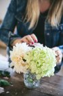 Happy lady near wooden table with bunches of fresh chrysanthemums, roses and plant twigs in vases on grey background — Stock Photo