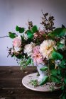 Концепція букета з сухих і свіжих троянд, хризантем і гілочок рослин у ретро вазі на дерев'яній дошці на сірому фоні — стокове фото