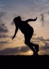 Silueta de mujer saltando en el fondo del cielo puesta del sol - foto de stock