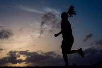 Silhouette of jogging woman on background of sunset sky — Stock Photo