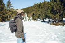Side view of young man in sunglasses and cap with backpack looking away between winter forest in Cerdanya, France — Stock Photo