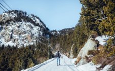 Back view of male walking on countryside road between mountains in snow in Cerdanya, France — Stock Photo