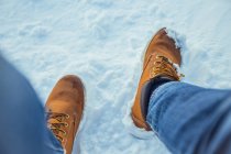 Crop male legs in jeans and winter boots sitting on snow in sunny day near hills in Cerdanya, France — Stock Photo