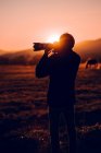 Vista posterior del macho tomando fotos de un hermoso paisaje entre colinas en un día soleado en Cerdanya, Francia - foto de stock