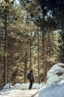 Junger Mann mit Sonnenbrille und Mütze mit Rucksack schaut weg, während er eine professionelle Kamera zwischen winterlichen Wäldern in Cerdanya, Frankreich, hält — Stockfoto