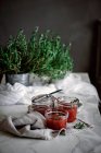 Piccoli vasi con deliziosi pomodori freschi marmellata fatta in casa vicino a erbe e tovagliolo sul tavolo su sfondo sfocato — Foto stock