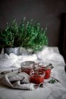 Vista superior de pequenos frascos com deliciosos tomates frescos compota caseira perto de ervas e guardanapo na mesa no fundo borrado — Fotografia de Stock