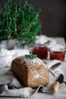 Delicious fresh aromatic rye bread on napkin near knife and cans with tomatoes homemade jam on blurred background — Stock Photo