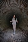 Mulher feliz com paus de trekking no túnel escuro — Fotografia de Stock