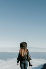 Visão traseira da mulher com câmera de foto em pé no topo da colina e olhando para a paisagem nublada — Fotografia de Stock