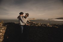 Vue latérale d'élégant couple élégant près des rochers sur la côte près de la mer et le ciel merveilleux — Photo de stock