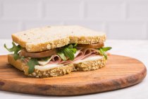 Delicious sandwich with ham, cheese and greens on wooden chopping board — Stock Photo