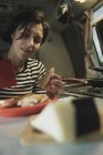Женщина за столом с блюдом из еды, сыра и столовых приборов принимая колбасу из горшка на плиту в мобильном доме — стоковое фото