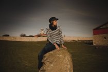 Elegant woman in cap sitting on stone — Stock Photo