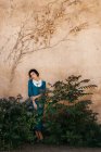 Mulher árabe atraente em vestido entre plantas perto da parede — Fotografia de Stock
