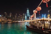 Lovely boat and crowded pier near rippling water at amazing night in brightly illuminated city of Dubai — Stock Photo