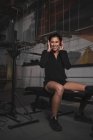 Vue latérale de la jeune femme en vêtements de sport avec écouteurs et gadget écouter de la musique et assis dans la salle de gym — Photo de stock