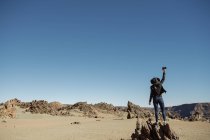 Touriste méconnaissable debout sur le sommet de la roche dans le désert dans une journée sans nuages — Photo de stock