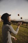 Елегантна жінка в кепці жонглює кульки на траві біля узбережжя моря і неба з сонцем — стокове фото