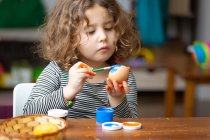 Маленькая девочка рисует яйцо за столом — стоковое фото