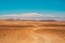 Живописный вид на сельскую дорогу между пустыней с дикими землями и голубым небом в Марракеше, Моро — стоковое фото