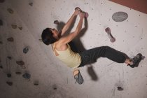 Visão traseira da mulher no treinamento de sportswear na parede de escalada com porões no ginásio — Fotografia de Stock