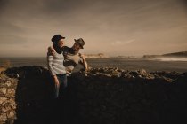 Вид збоку на стильну елегантну пару біля скель на узбережжі біля моря і чудове небо — стокове фото