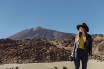 Fotógrafa feminina em pé com câmera e olhando para colinas no deserto — Fotografia de Stock