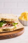 Delicioso sándwich con jamón, queso y verduras sobre tabla de cortar de madera con papas fritas - foto de stock
