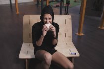Jeune femme en vêtements de sport avec des gâteaux de riz énergétiques assis sur le banc dans la salle de gym — Photo de stock