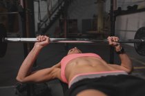 Femme en vêtements de sport faire des exercices avec des haltères sur banc de presse dans la salle de gym — Photo de stock