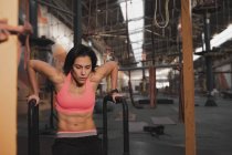 Femme en vêtements de sport faire des exercices pull up sur des barres parallèles dans une grande salle de gym — Photo de stock