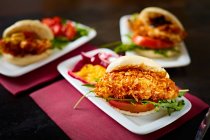 Appetizing burgers with tomatoes and crispy chicken on dark plates in gastrobar — Stock Photo