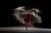 Young woman dancing and using powder in darkness — Stock Photo