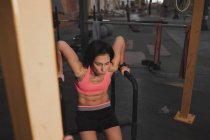 Mujer en ropa deportiva haciendo ejercicios pull up en barras paralelas en el gimnasio grande - foto de stock